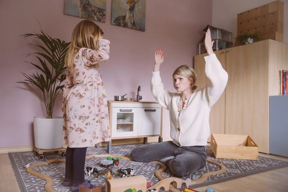 Logopädin und Mädchen heben im Therapieraum gemeinsam die Arme, eine Bewegungsübung